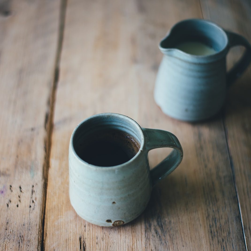 white ceramic mug with brown and white liquid inside on brown wooden surface